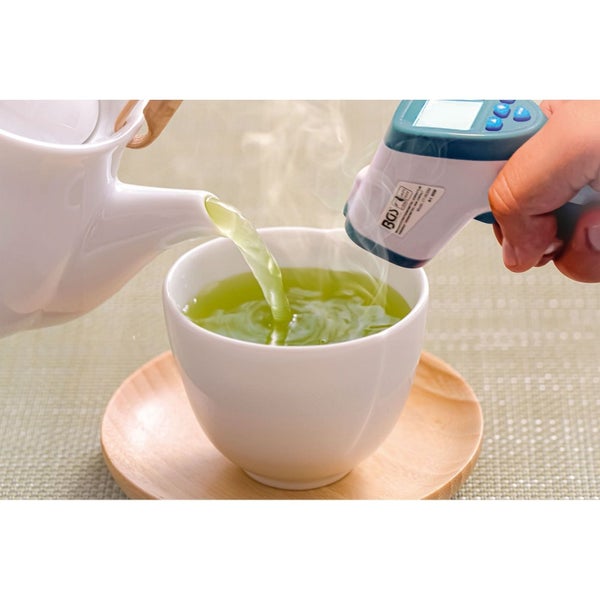 Eine Tasse wird mit einem Infrarotthermometer gemessen, während Tee aus einer Teekanne gegossen wird