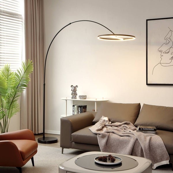 Moderne LED-Bogenstehleuchte mit rundem Leuchtkopf und schwarzem Gestell über einem braunen Sofa in einem hellen Wohnzimmer.