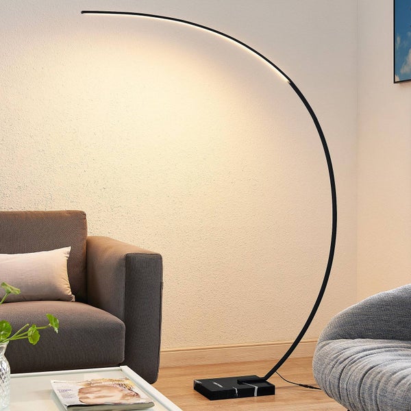Moderne schwarze LED-Bogenstehlampe mit Marmorsockel neben einem Sofa in einem hellen Wohnzimmer.