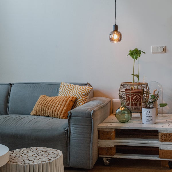 Wohnzimmer mit grauem Sofa, Kissen, Tisch aus Paletten, Lampe und Zimmerpflanzen.