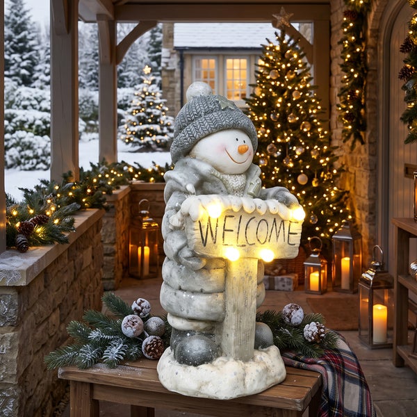 Dekorative Schneemannfigur mit LED beleuchtetem Willkommensschild für den Außenbereich auf einer überdachten Terrasse mit Weihnachtsbeleuchtung