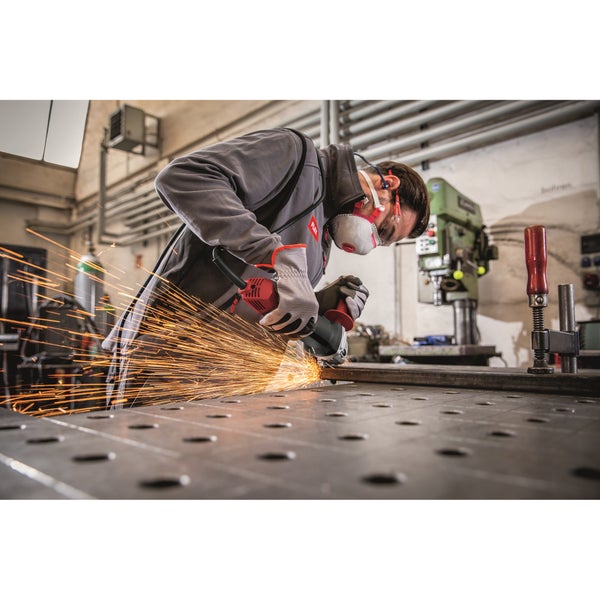 Ein Handwerker mit Schutzausrüstung trennt ein Metallprofil mit einem Winkelschleifer in einer Werkstatt und erzeugt dabei Funkenflug.