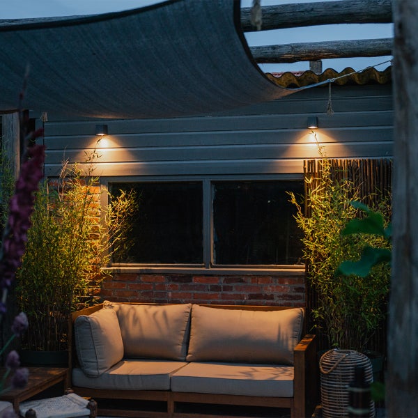 Gemütliche Terrasse mit Lounge-Sofa, Bambuspflanzen und stimmungsvoller Außenbeleuchtung unter einem Sonnensegel.