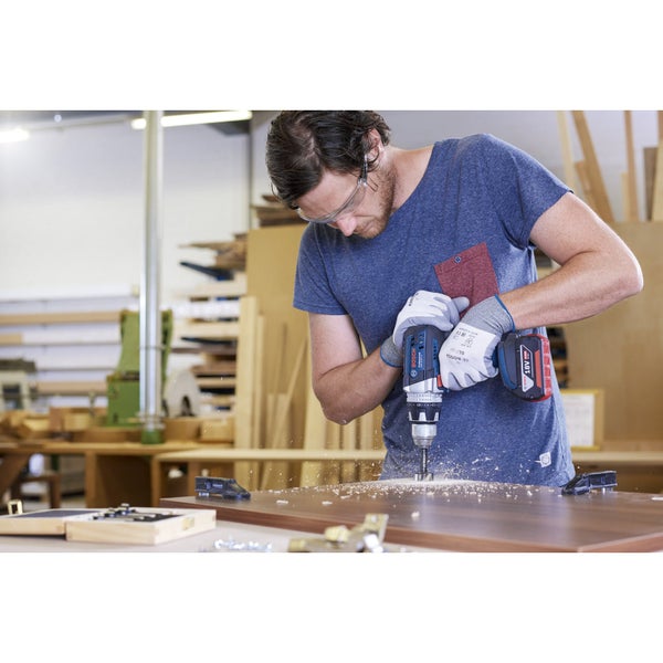 Mann bohrt mit einer Akku-Bohrmaschine ein Loch in ein Holzbrett