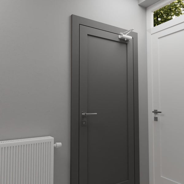 Ein moderner Türschließer ist an einer glatten Innentür mit Metallbeschlag montiert, platziert in einem hellen Innenraum mit Heizkörper.