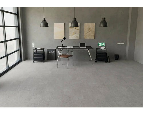 Modernes Büro mit Bodenbelag in grauer Steinoptik, schwarzem Schreibtisch, Industrie-Pendelleuchten und Wänden in Betonoptik.
