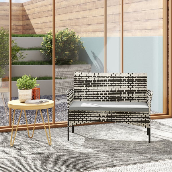 Moderne Gartenecke mit schwarz-weiß geflochtener Gartenbank, grauem Sitzkissen und rundem Beistelltisch aus Holz in heller Umgebung.