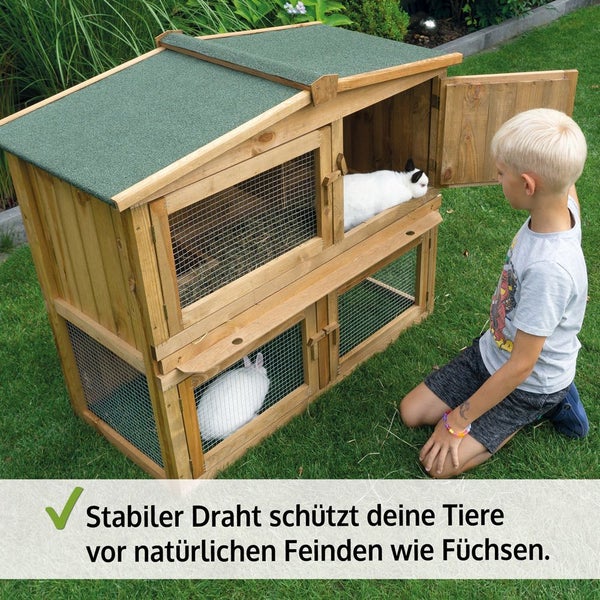 Zweistöckiger Kaninchenstall aus Holz mit grünem Dach und stabilem Drahtgeflecht zum Schutz vor Raubtieren, ein Kind kniet im Garten daneben.