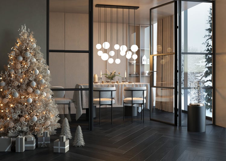 Festlich dekorierter Raum mit verschneitem Weihnachtsbaum, Geschenken und Blick durch Glastüren in ein Esszimmer mit moderner Pendelleuchte.