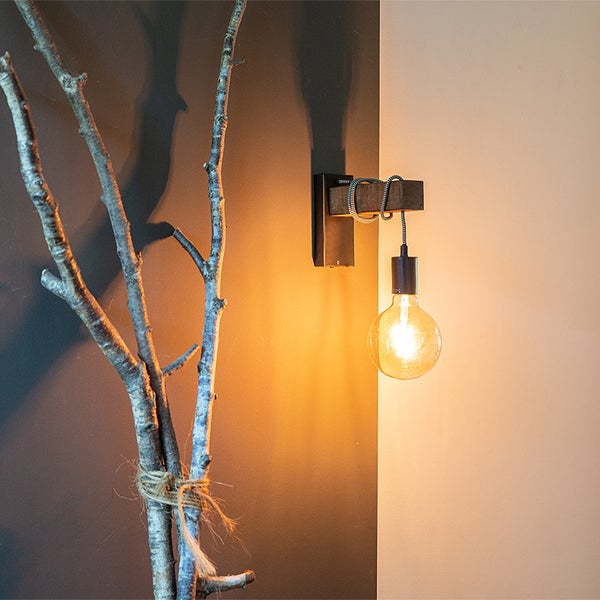 Wandleuchte aus Holz mit Glühbirne neben einem dekorierten Ast