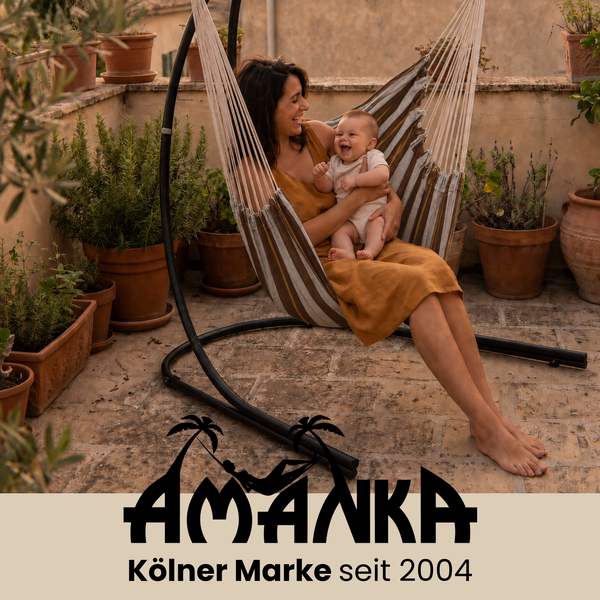 Frau mit Baby in einem gestreiften Hängesessel auf einer Terrasse mit vielen Pflanzen. Amanka Logo.