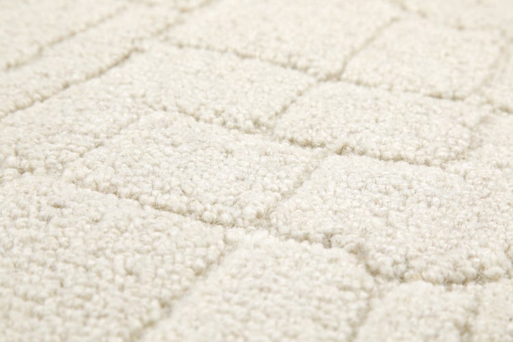 Nahaufnahme eines hellen Teppichs mit quadratischem Reliefmuster und weicher Textur.