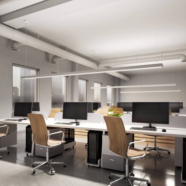 Moderne Bürobeleuchtung mit einer langen, schmalen LED-Pendelleuchte über Schreibtischen in einem hellen, organisierten Großraumbüro.