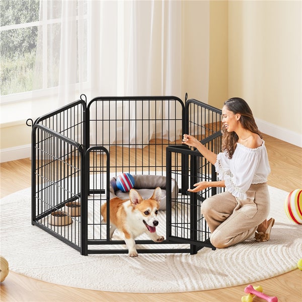 Eine Frau kniet neben einem schwarzen Metall-Hundeauslaufgehege mit einem Hund, einem Hundebett und Spielzeug.