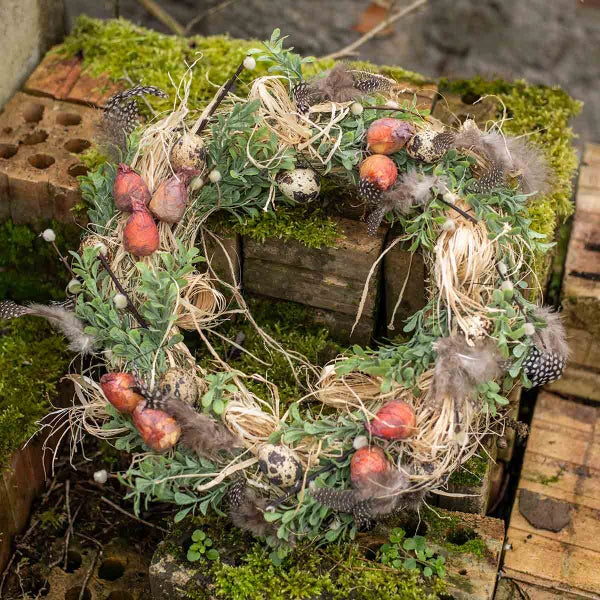Dekorativer Kranz mit Federn, Eiern und Pflanzen auf Backsteinen