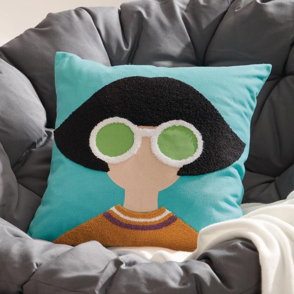 Dekokissen mit Frauenporträt und Sonnenbrille auf einem grauen Sessel.