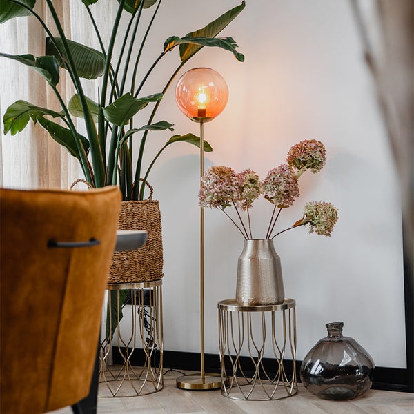 Dekoratives Wohnambiente mit Stehlampe, Pflanzen und Vasen auf Beistelltischen