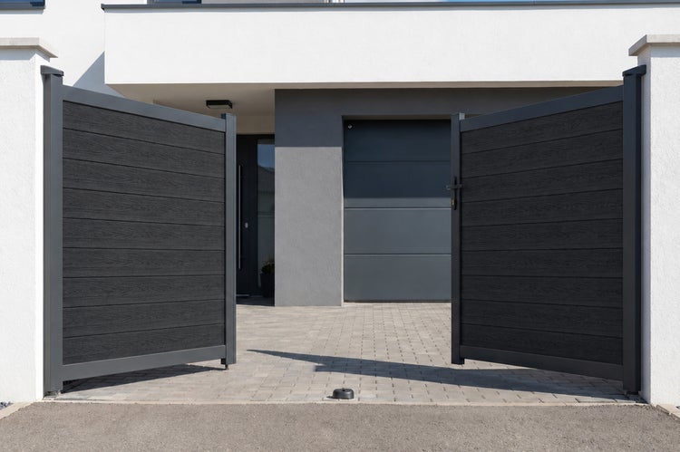 Modernes zweiflügeliges Einfahrtstor aus Holz-Kunststoff-Verbundwerkstoff in Anthrazit mit Holzmaserung und Aluminiumrahmen auf gepflasterter Einfahrt.