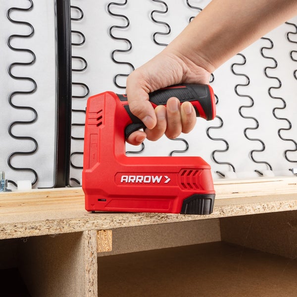 Hand bedient roten Arrow Tacker auf Holzplatte. Im Hintergrund sind Wellenfedern für Möbel sichtbar.