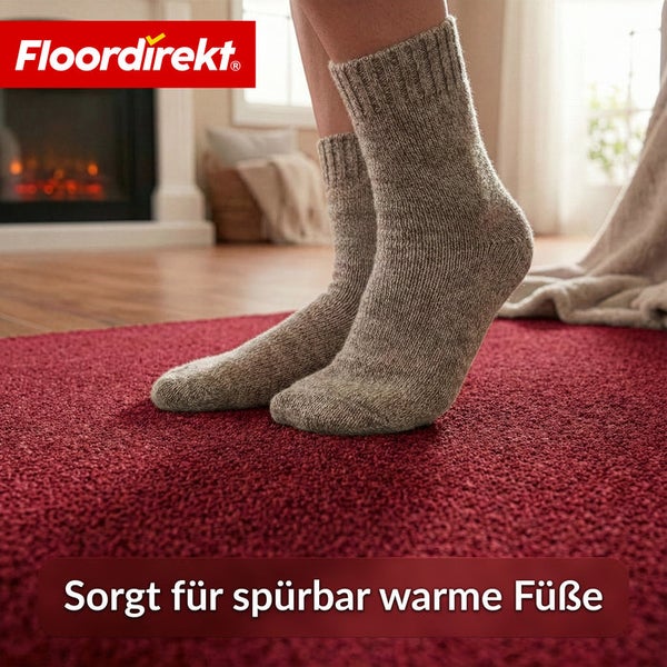 Person mit Wollsocken steht auf einem roten Teppich vor einem Kamin.