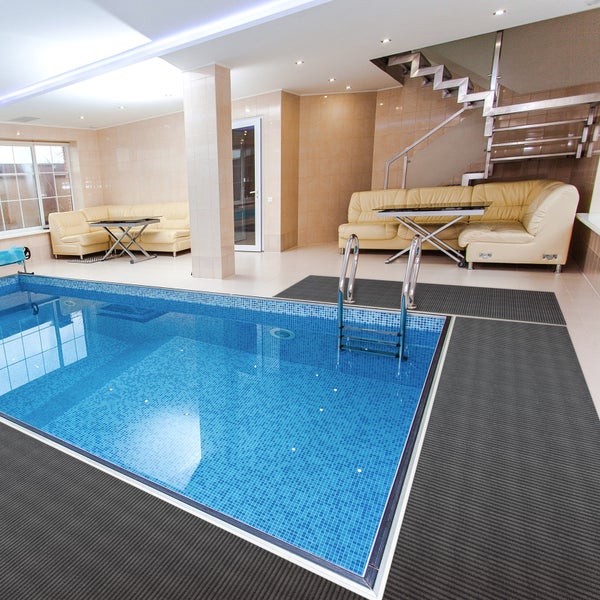 Modernes Hallenbad mit blauen Mosaikfliesen, Edelstahlleiter, grauen Antirutschmatten und Lounge-Bereich mit Ledersofas.