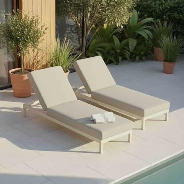 Zwei moderne Gartenliegen mit hellen Polstern auf einer gefliesten Terrasse am Pool, umgeben von Pflanzen in Töpfen.