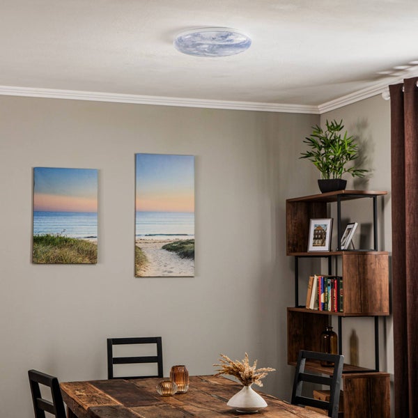 Runde Deckenleuchte mit Erd-Motiv in einem modern eingerichteten Esszimmer mit Holzmöbeln und Wandbildern.