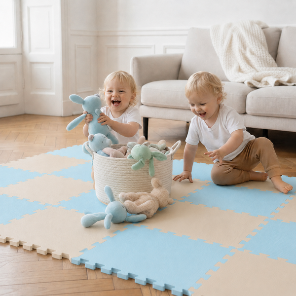 Zwei kleine Kinder spielen auf einer weichen Spielmatte aus Schaumstoffpuzzleteilen mit Stofftieren in einem hellen Wohnzimmer.