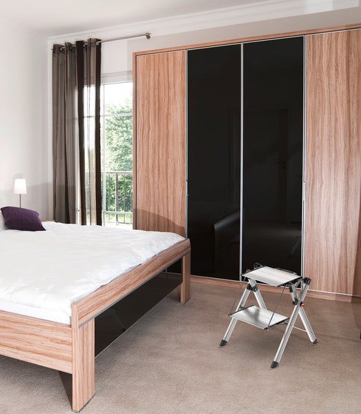 Schlafzimmer mit Bett, Schrank und silberfarbener Trittleiter