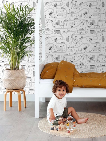 Kindertapete mit Straßenmuster in einem eingerichteten Kinderzimmer mit einem Kind das auf einem Teppich spielt