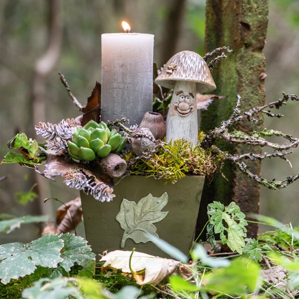 Dekorative Herbstszene mit Kerze, Pilzfigur und Pflanzen in einem Topf.