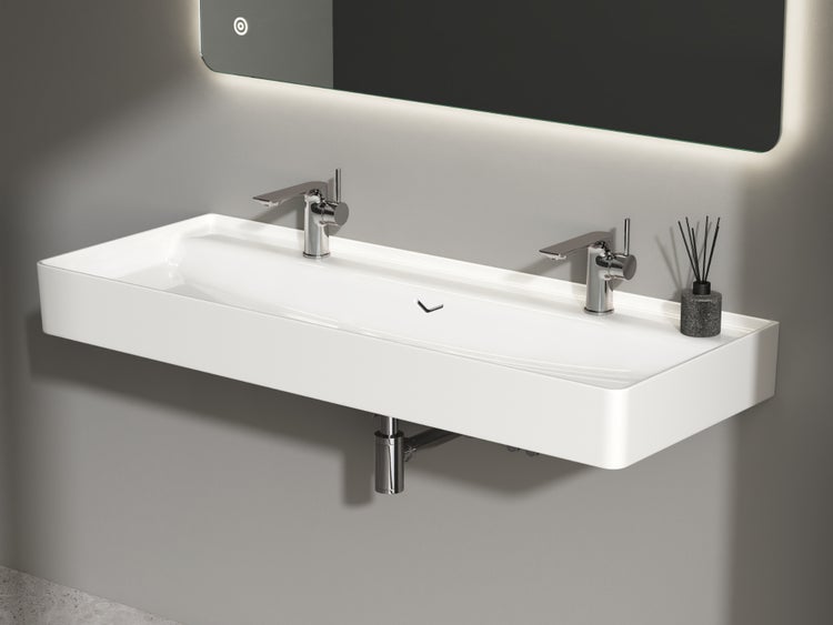 Modernes, rechteckiges Doppelwaschbecken aus Keramik mit zwei verchromten Armaturen an einer Wand montiert in einem hellen Badezimmer.