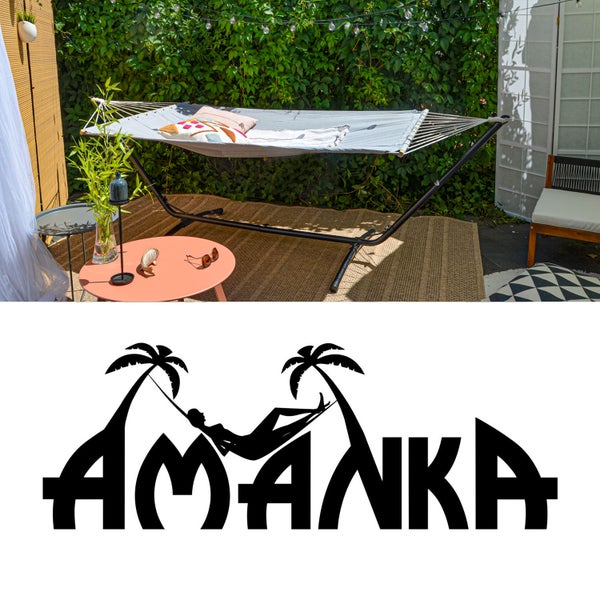 Graue Stabhängematte mit schwarzem Metallgestell in einem Garten mit Hecke auf einem Outdoorteppich. Amanka Logo.