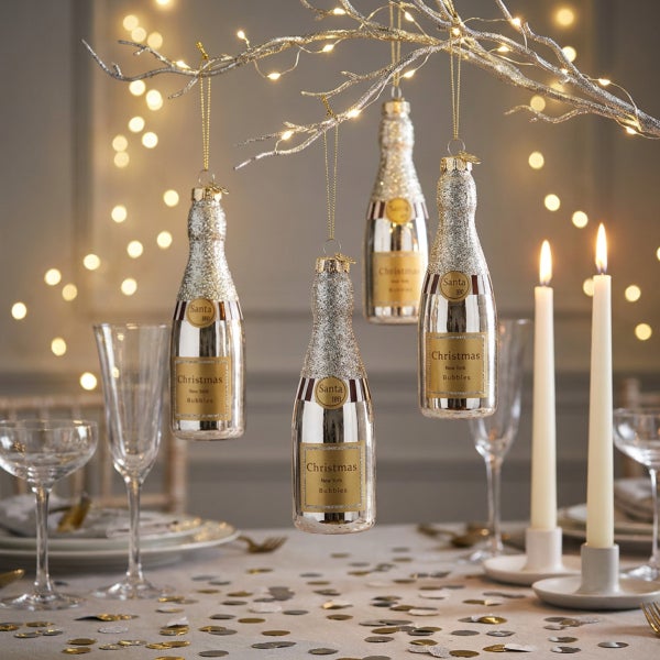 Weihnachtsbaumschmuck in Form von Champagnerflaschen haengend an einem beleuchteten Zweig als festliche Tischdekoration.