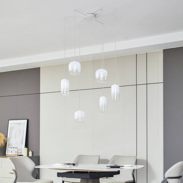 Sechsflammige Pendelleuchte mit zylindrischen Glasschirmen in verschiedenen Höhen über einem Esstisch in einem hellen, modernen Esszimmer.