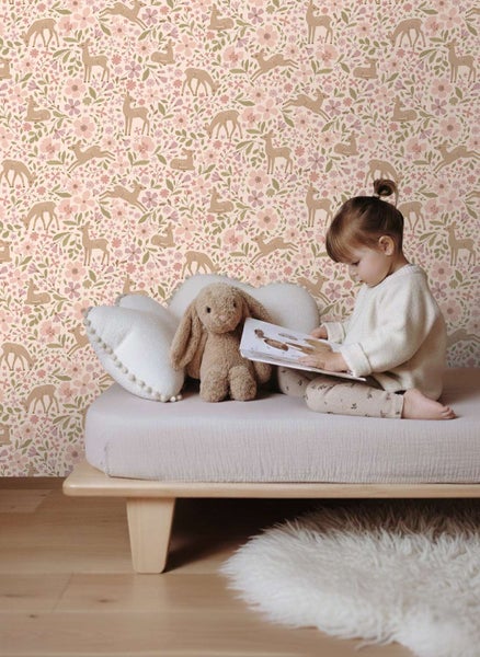 Kind liest Buch auf einem Bett vor einer Tapete mit Blumen und Rehen in einem Kinderzimmer