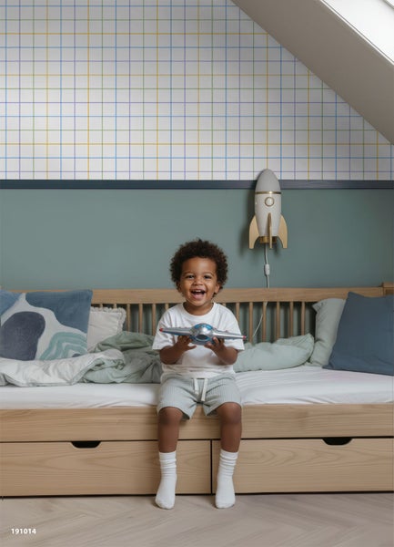 Kinderzimmer mit Vliestapete im Karomuster, Holzbett mit Schubladen und Raketenlampe an der Wand.