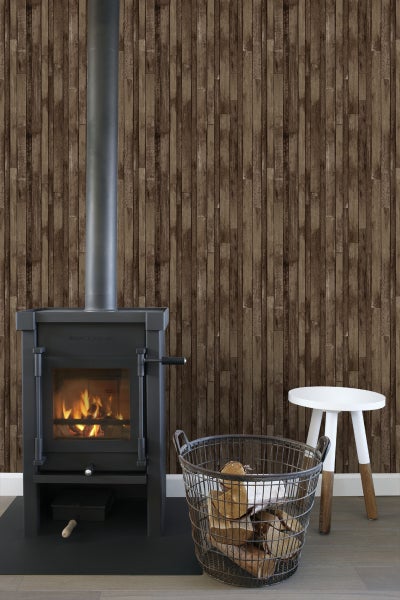 Szene mit Kaminofen, Brennholzkorb und Hocker vor einer Wand mit Holzpaneel-Tapete.