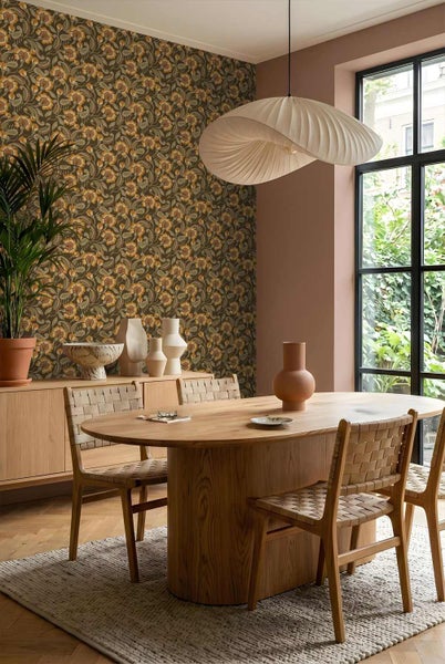 Helles Esszimmer mit floraler Tapete, ovalem Holztisch, Flechtstühlen und skulpturaler Pendelleuchte auf einem Teppich.