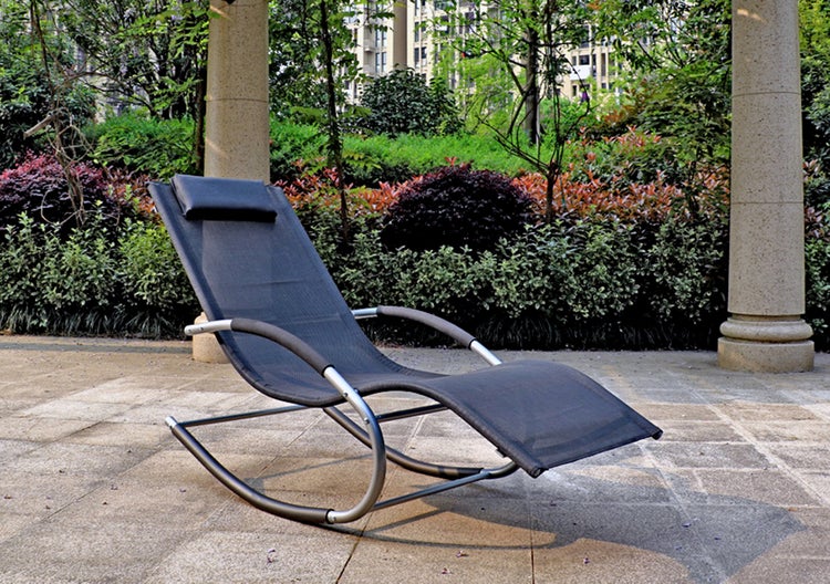 Ergonomische Garten-Schaukelliege mit geschwungenem Metallgestell, dunklem Textilgewebe und Kopfpolster auf einer Steinterrasse im Garten.
