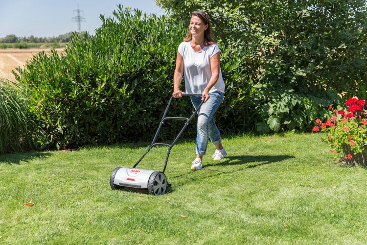 Eine Frau nutzt einen AL-KO Handrasenmäher im Garten, um das Gras auf einer Rasenfläche zu schneiden.