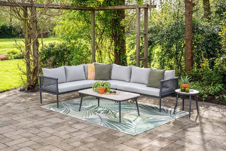 Eckige Gartenlounge mit hellgrauen Polstern, Couchtisch und Beistelltisch auf einem grünen Outdoor-Teppich unter einer Pergola.