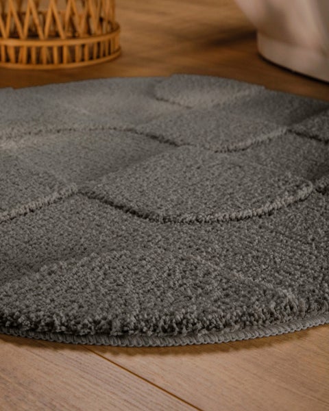 Grauer runder Badeteppich mit strukturiertem Hoch-Tief-Muster aus weichem Flor auf Holzboden.