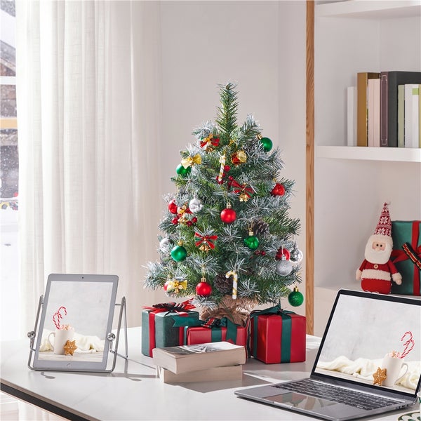 Dekorierter Weihnachtsbaum mit Geschenken auf einem Tisch mit Laptop und Tablet.
