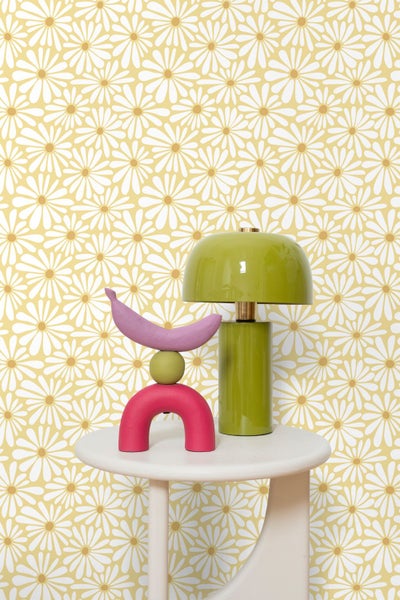 Tapete mit floralem Gänseblümchen-Muster, davor ein Beistelltisch mit einer grünen Tischlampe und einer bunten abstrakten Skulptur.