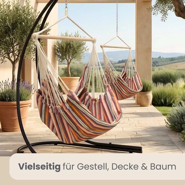 Gestreifter Hängesessel auf einer Terrasse, befestigt an einem Metallgestell und an der Decke, umgeben von Pflanzen.