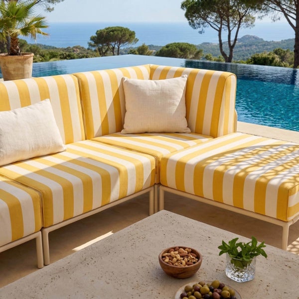 Modulares Gartensofa mit gelb-weiß gestreiften Polstern und hellen Kissen an einem Pool mit Meerblick.