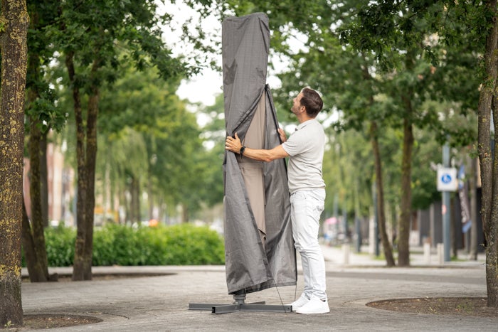 Mann öffnet eine Schutzhülle eines Sonnenschirms im Außenbereich.