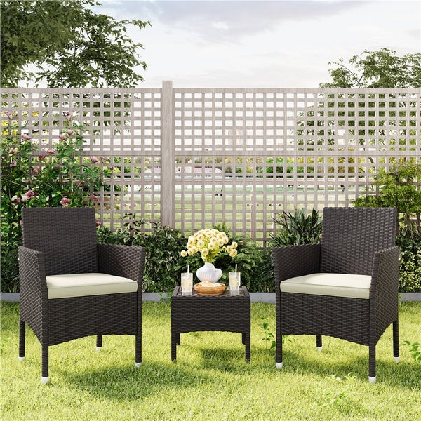 Gartenmöbel-Set aus Polyrattan mit zwei Sesseln inklusive Sitzkissen und einem Beistelltisch vor einem Holzspalierzaun im Garten.