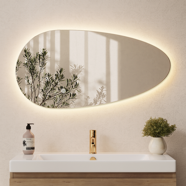Organisch geformter Badezimmerspiegel mit indirekter LED Beleuchtung, montiert über einem Waschtisch mit Armatur in Holzoptik.
